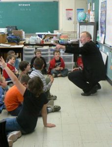 An older man gestures in front of a group of students in a classroom