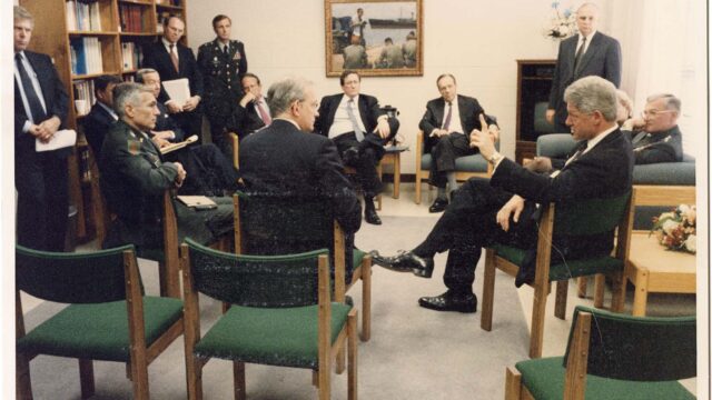 Clinton sits in a room with other government officials in a circle