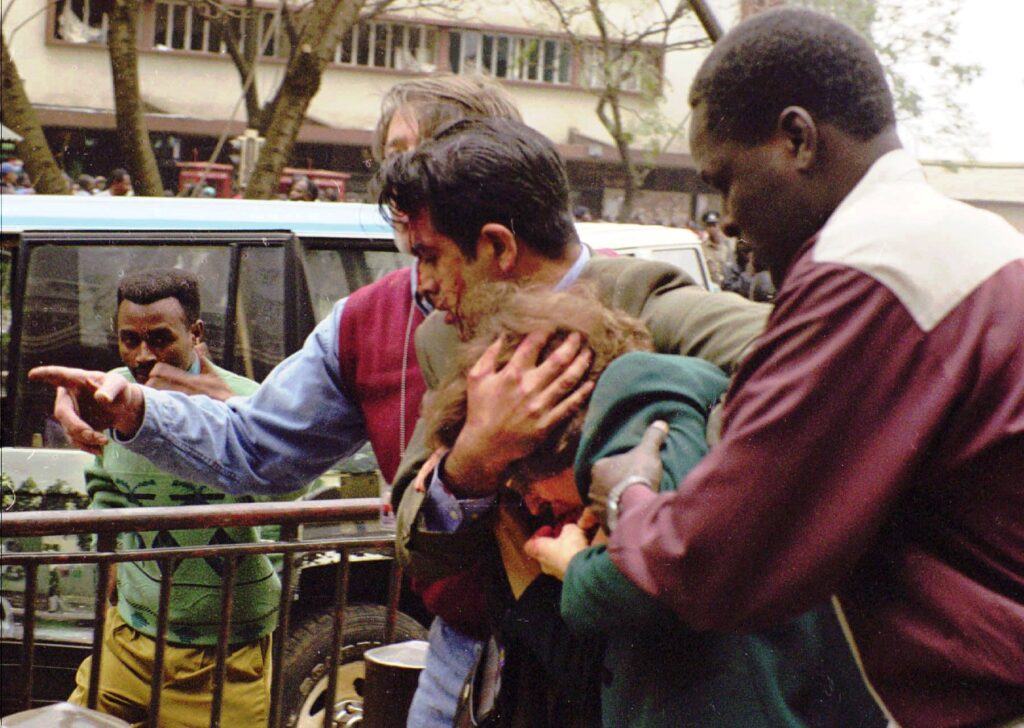 U.S. Commercial Officer Riz Khaliq shields Ambassador Bushnell as Foreign Service National George Mimba (right) and Foreign Service Officer Steve Nolan (left) assist in evacuating the ambassador from the site.