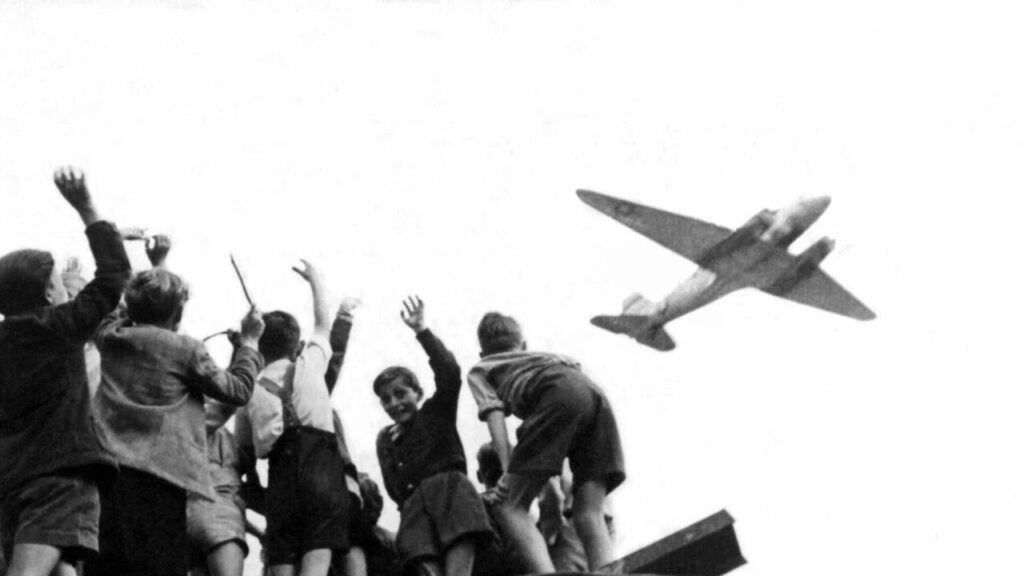 A group of children wave at a plane, black and white