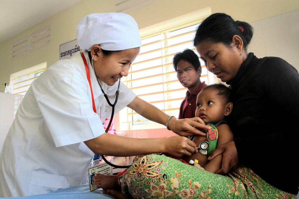 A Cambodian nurse holds a stethoscope to a baby.