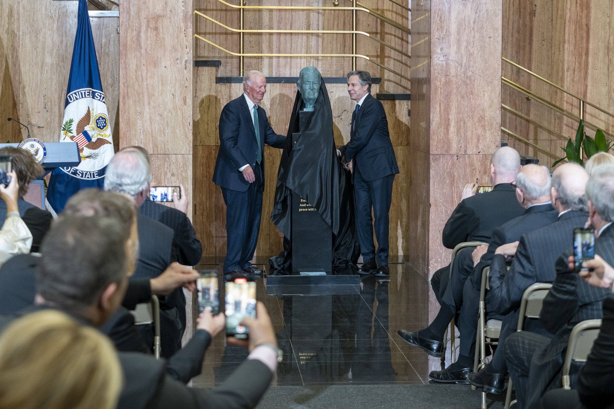 James Baker and Antony Blinken take a veil off of a bronze bust of James Baker in front of an audience