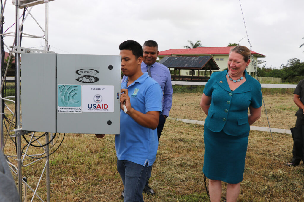 Ambassador Karen Williams stands smiling looking at a weather station with two others