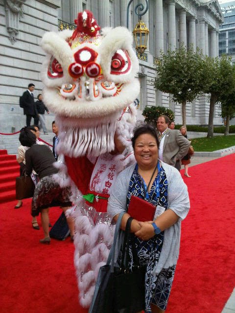 A woman stands holding a folder in front of a person wearing a traditional dragon costume on a red carpet