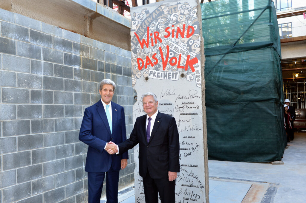 John Kerry in front of the signature segment of the berlin wall