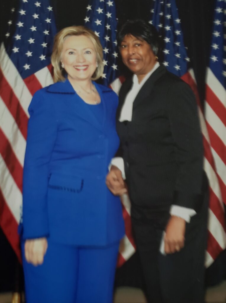 Scan of a photograph of Claudia standing with Hillary Clinton
