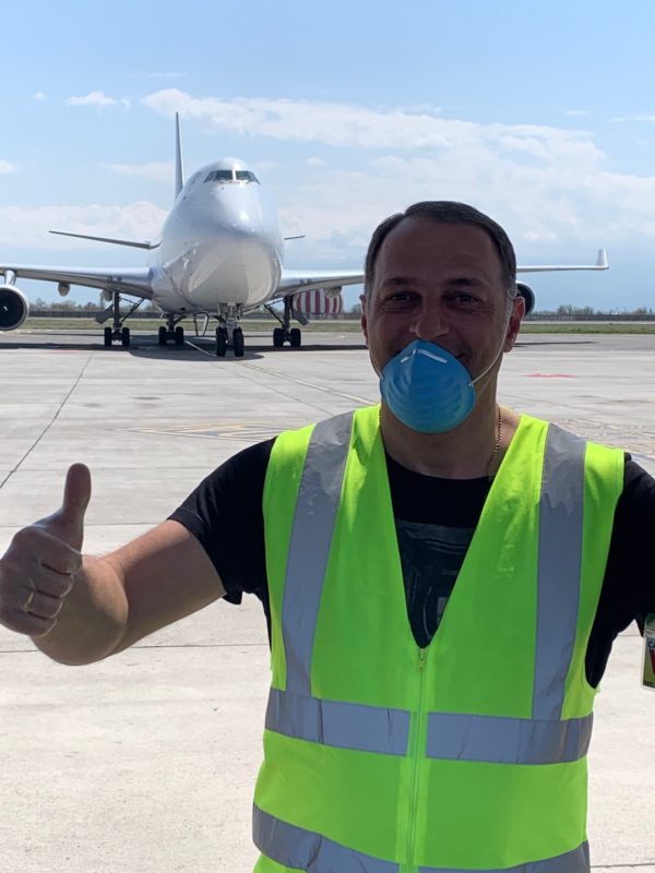 Person in yellow vest gives a thumbs up in front of a plane