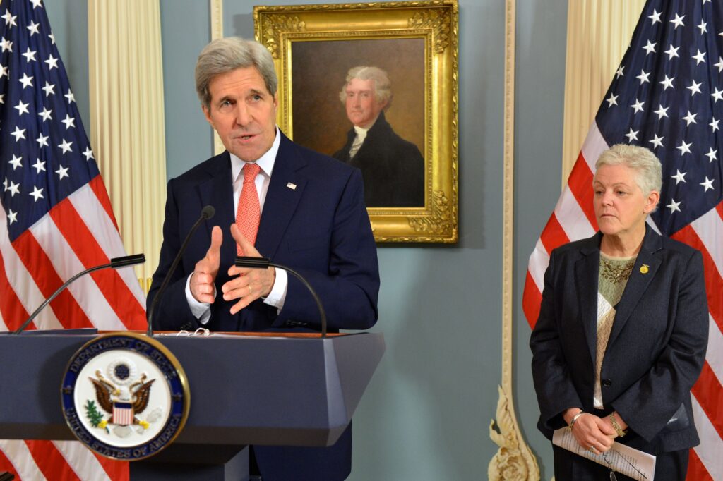 Then U.S. Secretary of State John Kerry standing at a podium in front of two American flags while Administrator of the U.S. Environmental Protection Agency stands to the right.