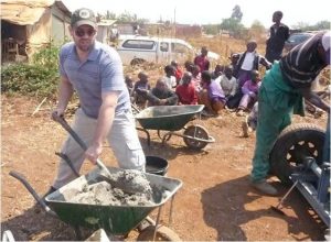 A man removes material from a wheelbarrow with a group of people in the background