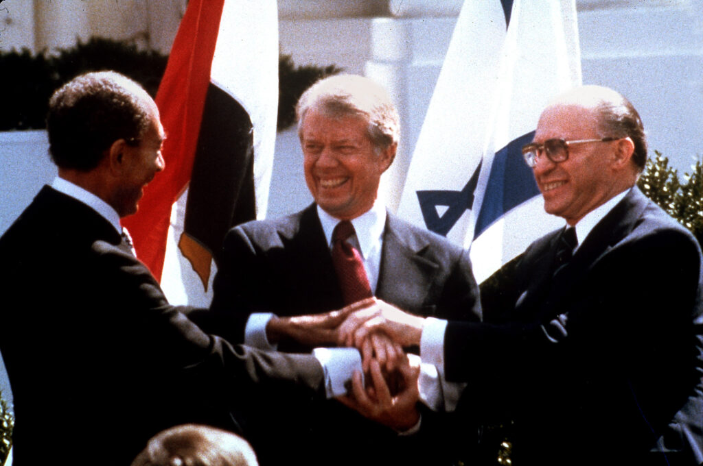 Carter, Sadat, and Begin shake hands in front of flags