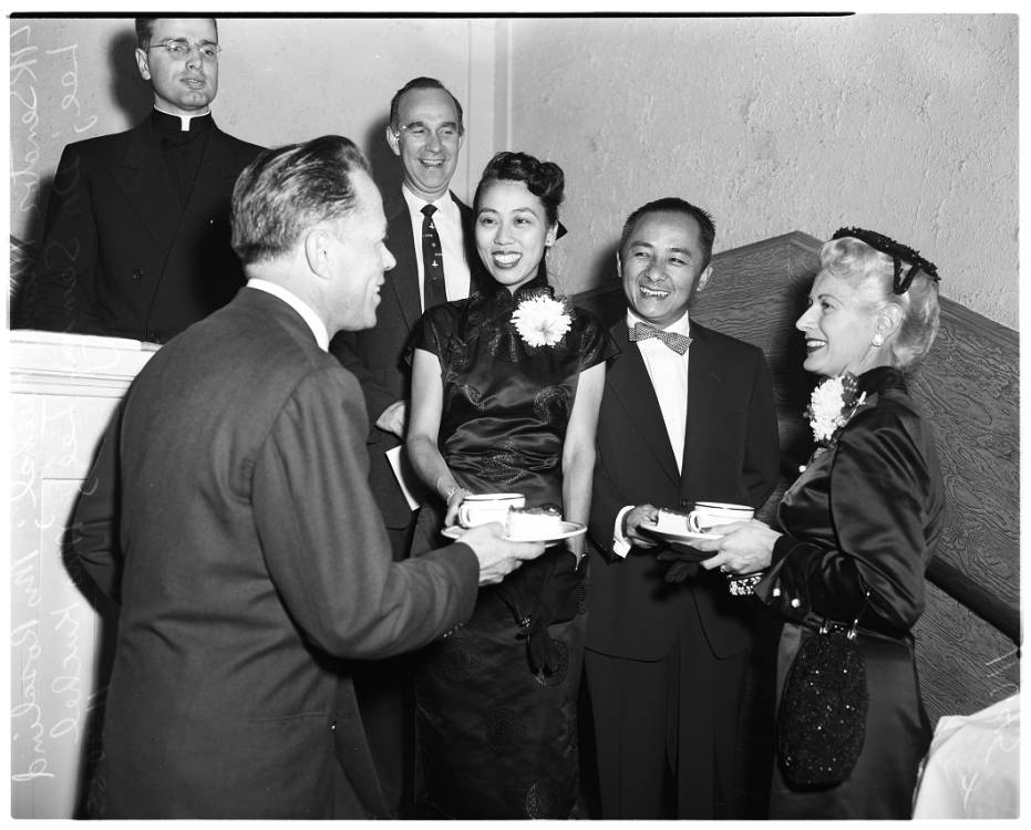 Un grupo de personas con atuendo formal conversando en una escalera, imagen en blanco y negro