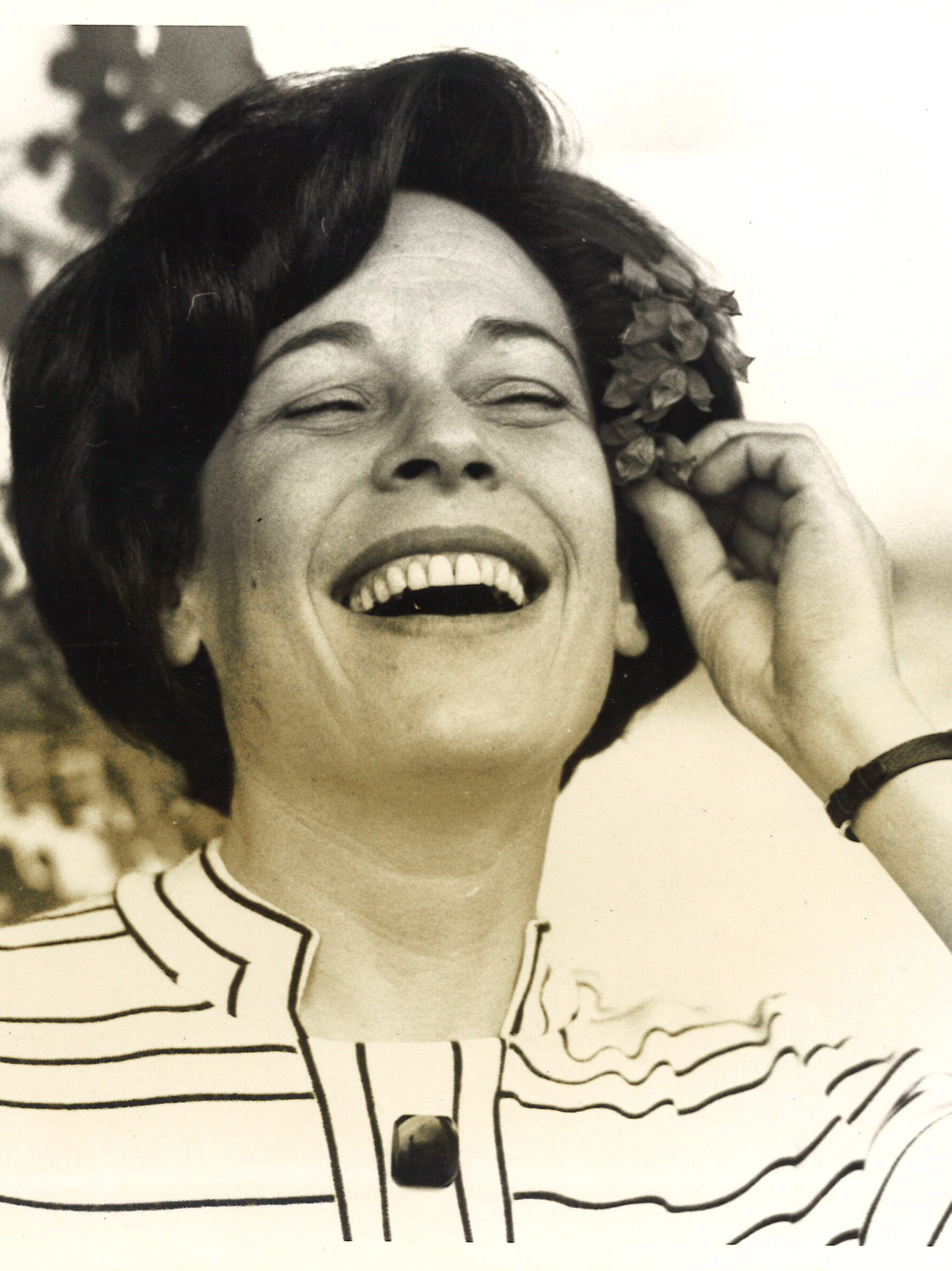 A woman in a striped shirt smiles with flowers in her hair.