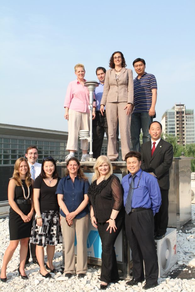 Erica Keen Thomas poses with 10 other coworkers by standing on top of an Air Monitor on a roof in Beijing.