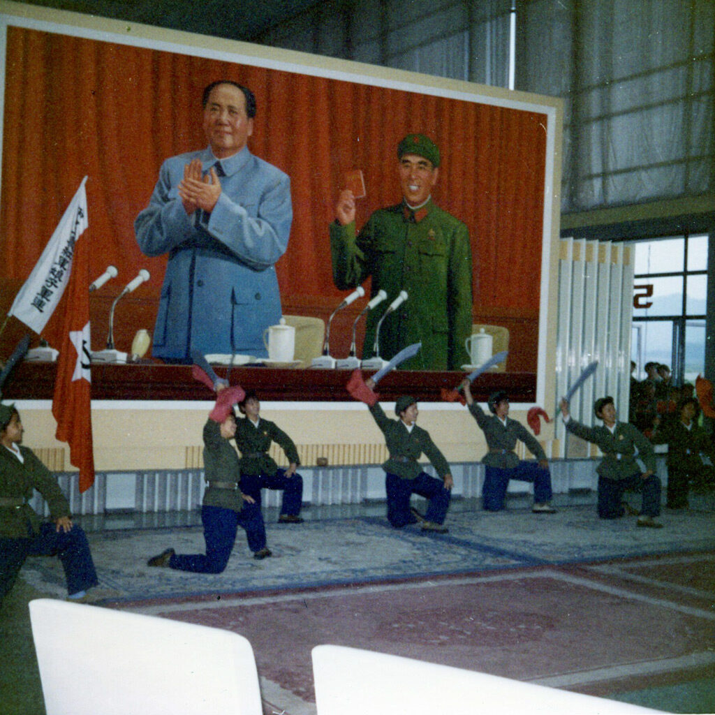 A dance troupe in front of a stage and a mural of government leaders