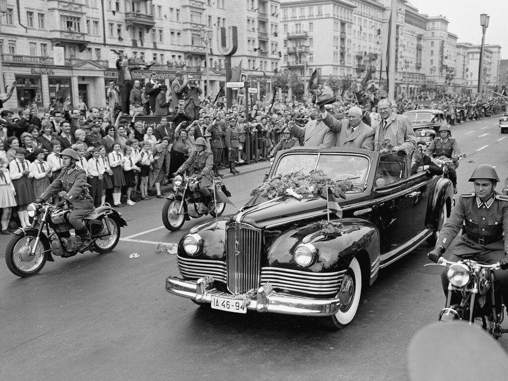 Soviet Prime Minister Nikita Khrushchev waves his hat from his open car to welcoming crowds along the Stalin-Alee in Communist East Berlin, Germany. Khrushchev is flanked by Walter Ulbricht, left, chief of the East German Communist Party, and Otto Grotewohl, the East German Prime Minister. May 19, 1960. AP photo.