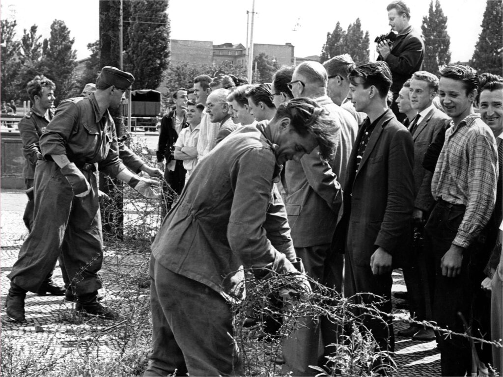 East German soldiers, left, set up barbed wire barricades August 13, 1961, at the border separating Berlin, Germany, to restrict the travel between the eastern and western part of the German city. West Berlin citizens, right, watch the work.