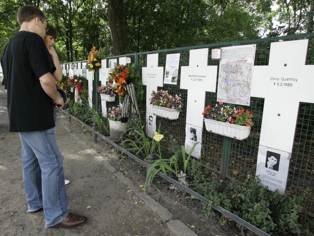 Tourists look at the remembrance crosses for the victims the East German police killed while trying to cross the Berlin Wall, August 13, 2007, in Berlin near the Reichstag (German Parliament Building). AP photo.