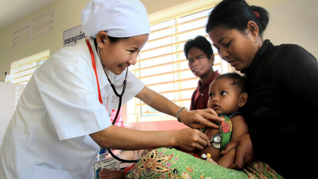 A Cambodian nurse holds a stethoscope to a baby.