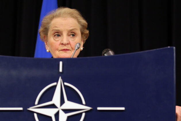 Secretary Albright stands in front of a podium with the NATO logo