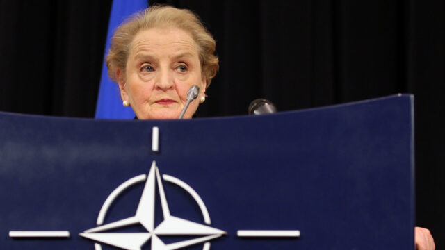 Secretary Albright stands in front of a podium with the NATO logo