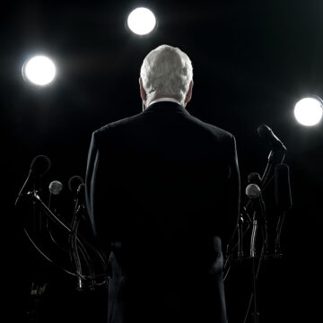 A man stands in front of a podium with microphones