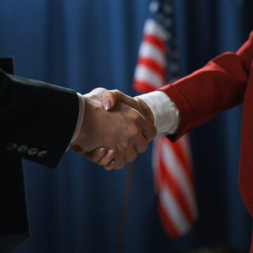 Two people shaking hands in front of an American flag