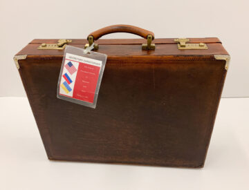 A brown leather briefcase with a tag that says “Secretary Christopher: The Trip of President Clinton to Moscow and Kiev May 8-12, 1995”