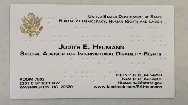 A business card with text and Braille characters.