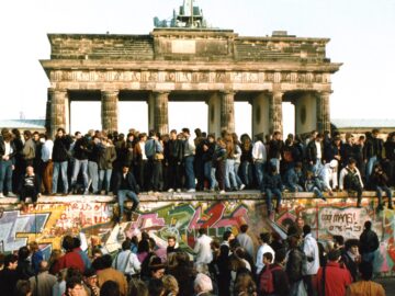 People lined the top of the Wall in 1989 with the Brandenburg Gate in the background as a crowd gathered below.