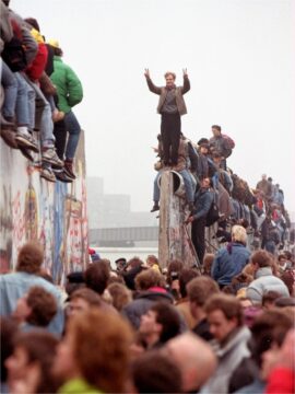 A man atop the Wall raises his arms in triumph in 1989 as people below surge through a breach in the barricade.