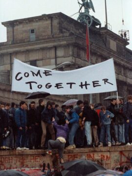 East Germans atop the Berlin Wall in 1989 display the sign in English, “COME TOGETHER.”