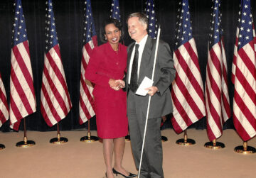 Avraham Rabby standing next to Secretary Rice in front of American flags