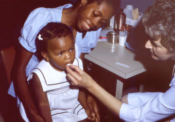 a woman gives a small child a sugar cube with a polio vaccine