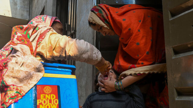 a woman gives a child a polio vaccine in front of a cooler that says end polio now