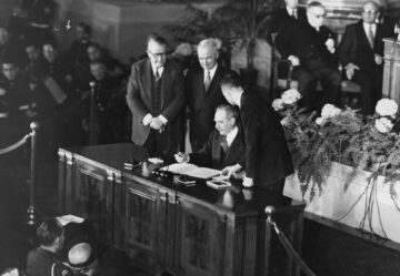 President Truman and Dean Acheson sign the North Atlantic Treaty on a desk in front of an audience