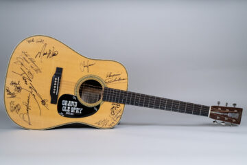 A wooden acoustic guitar covered with autographs in black ink.