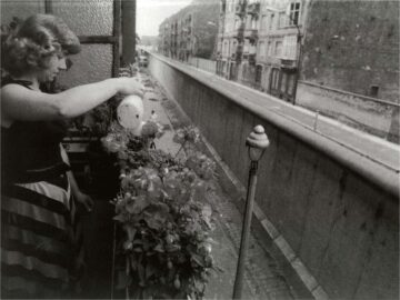 Foto: eine Frau gießt auf ihrem direkt hinter der Berliner Mauer gelegenen Balkon die Blumen
