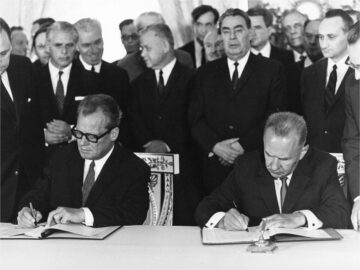 Foto: Am Tisch Bundeskanzler Willy Brandt und der sowjetische Premierminister Alexej Kosygin bei der Unterzeichnung des Moskauer Vertrags, hinter ihnen stehen viele Männer