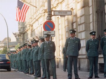 Foto: Volkspolizisten stehen in einer langen Reihe vor einem Gebäude mit amerikanischer Flagge