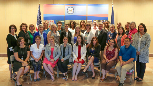 A group of teachers pose in front of a NMAD backdrop