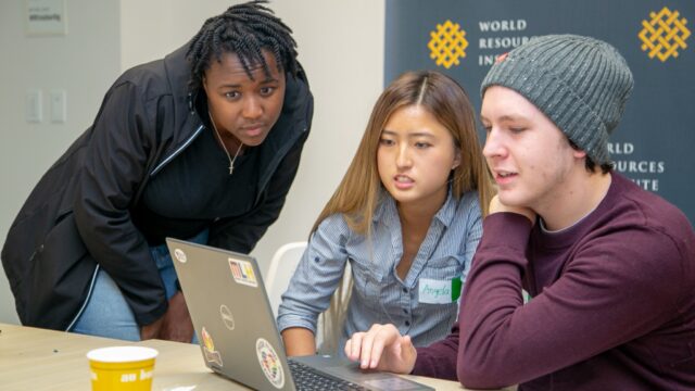 Three people look at a laptop computer and speak to each other.