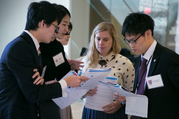 A group of college-age students in a huddle, holding papers