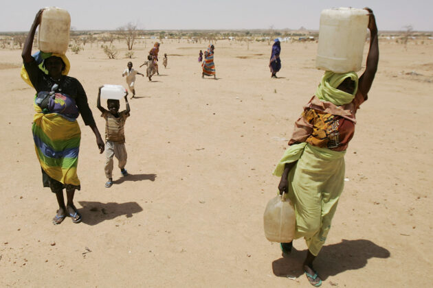 Photograph of women and children carrying jugs of water balanced on their heads.
