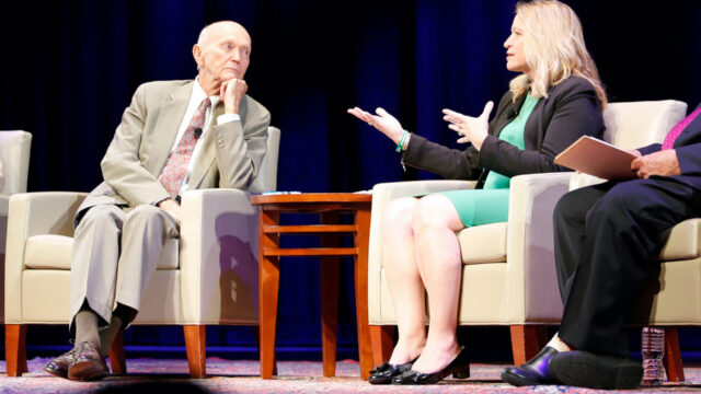 Michael Collins listens to Dr. Ellen Stofan speak and gesturing with hands