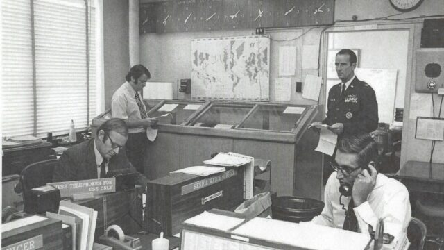 Black and white photo of four men working in an office