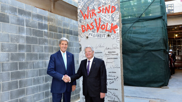 John Kerry in front of the signature segment of the berlin wall