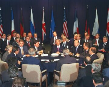 A group of men sitting around a table with flags in the background at the dayton accords