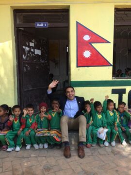 Greg Pardo sitting outside a school in Nepal with school children.