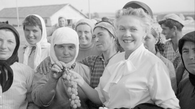 Eugenie Anderson stands with a bunch of farmers in Bulgaria as one hands her grapes.