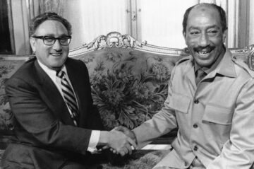 Black and white photo of Kissinger and Sadat shaking hands on a couch.